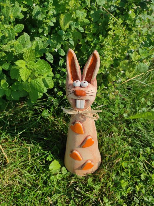Keramický zajíc se čtyřmi oranžovými srdíčky a lýkovou mašlí.